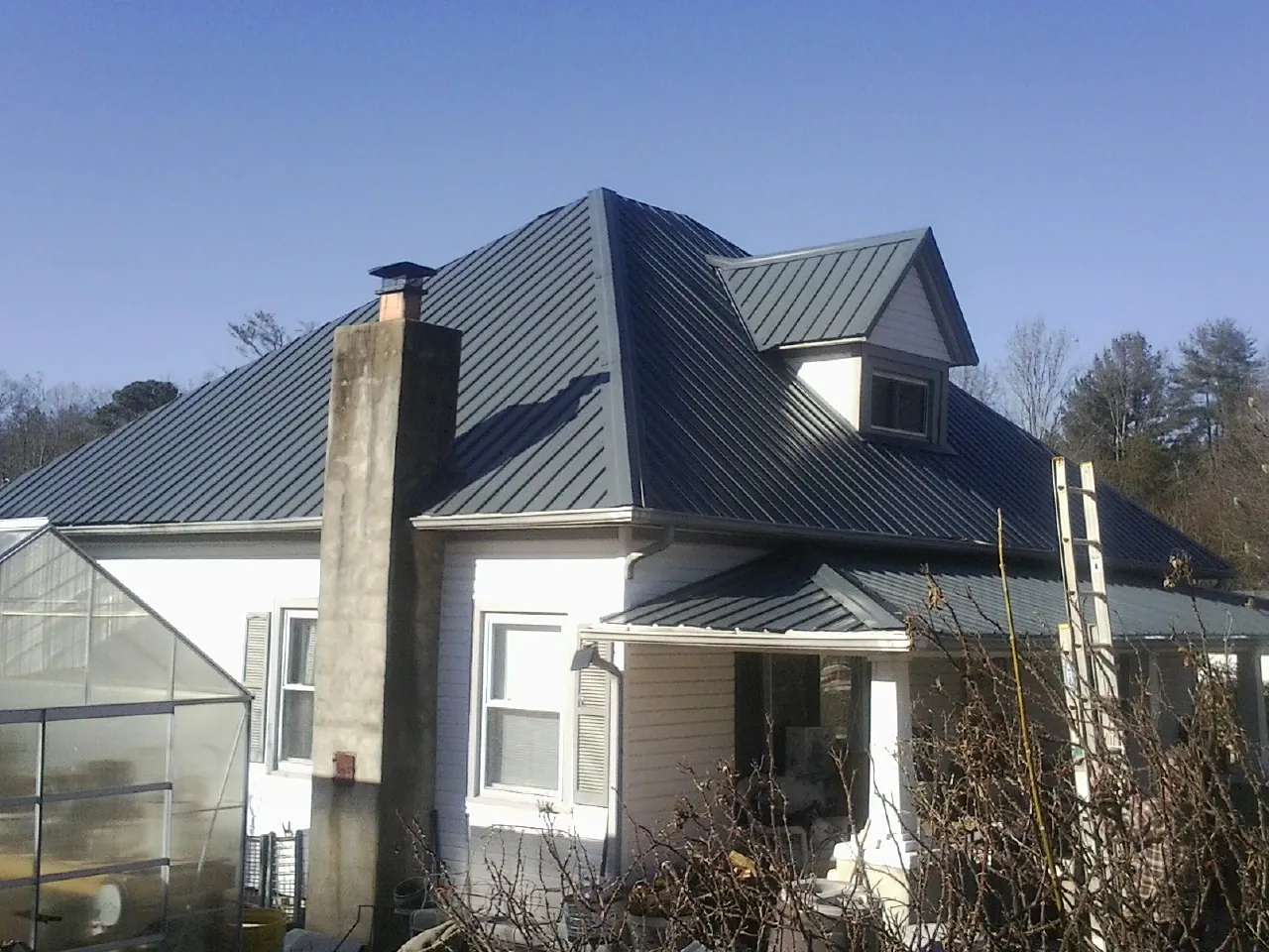 Dark blue standing seam metal roof on a white farmhouse with dormer — Slate & Tile Roof Repair by Roofing Brothers in Winnett