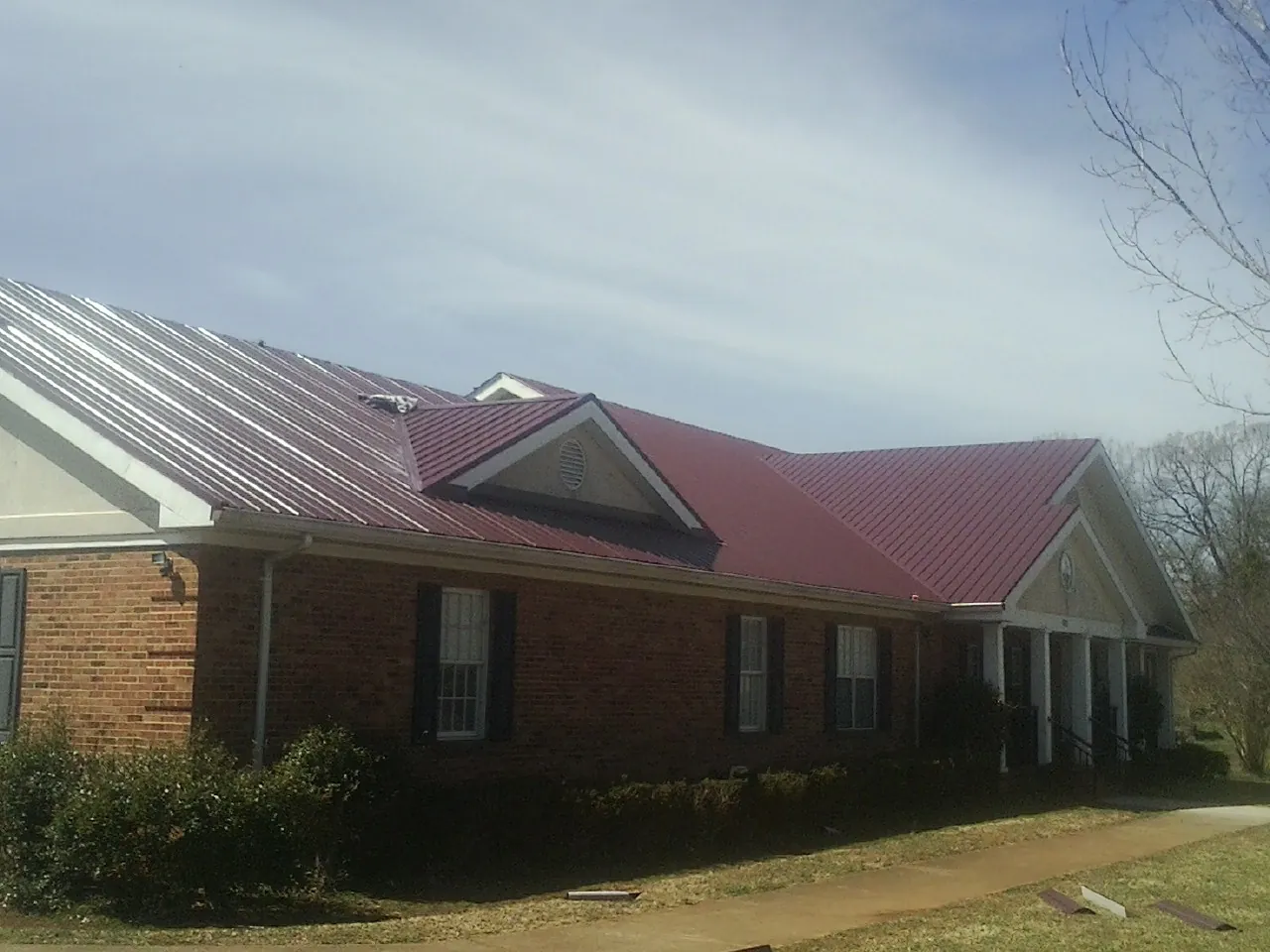 Red metal roof with gabled entries on a long brick building, from a Hail Damage Roof Repair job in Winnett