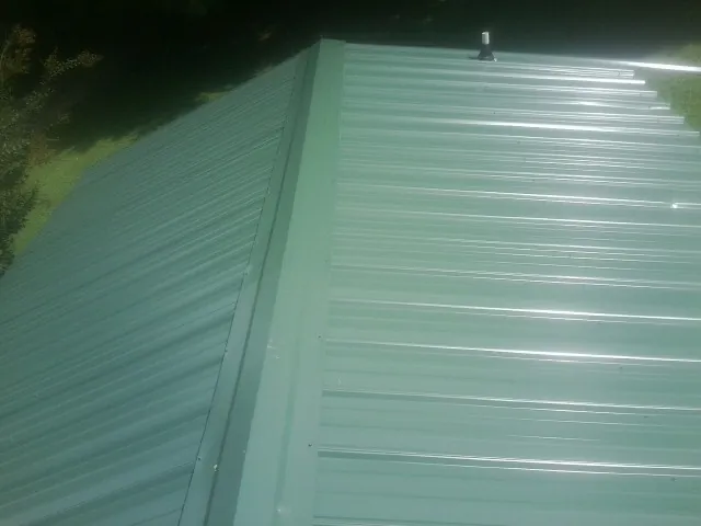 New green metal panels meeting at the ridge of a roof — Flat Roof Repair work by our crew in Winnett