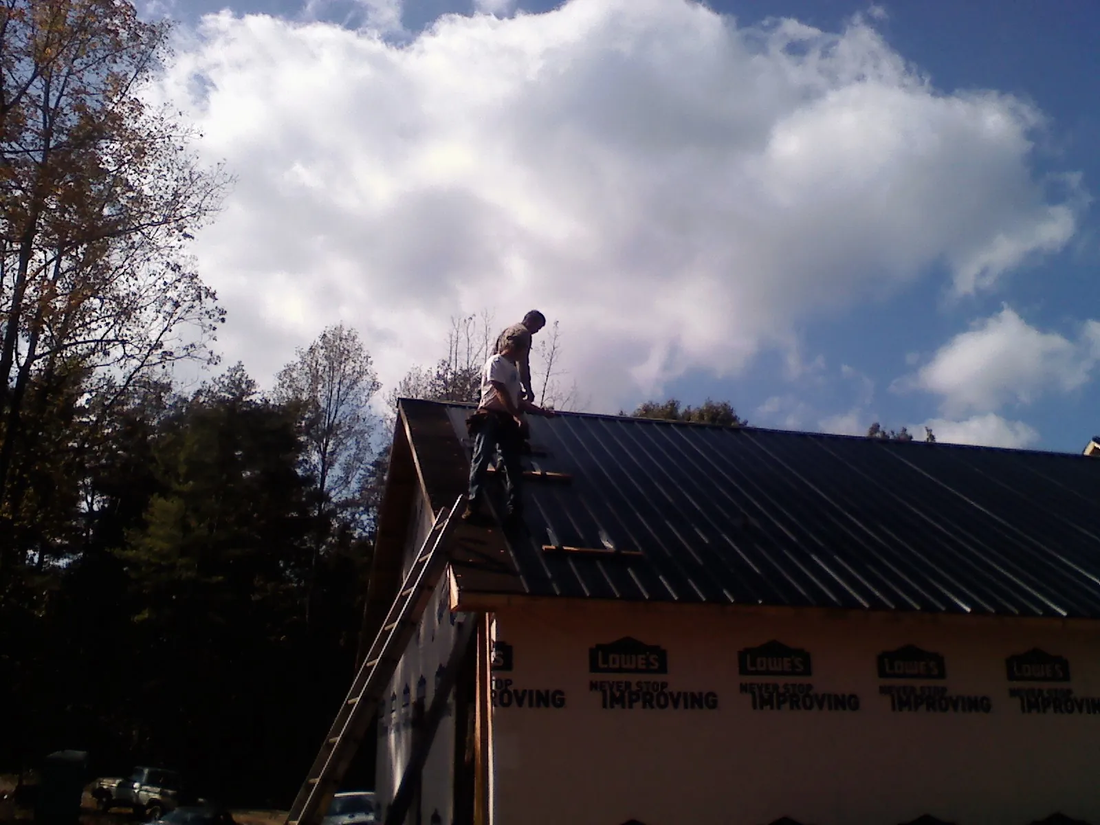 Roofer fastening dark metal panels high against a cloudy sky, from a Roof Inspection job in Winnett