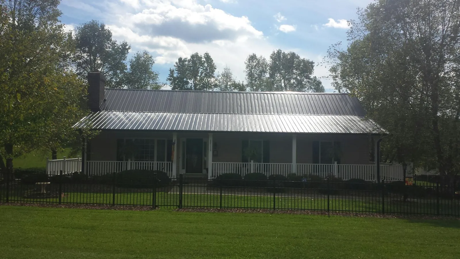 Gray metal roof on a brick ranch with a full width front porch — Gutter Guard Installation work by our crew in Winnett