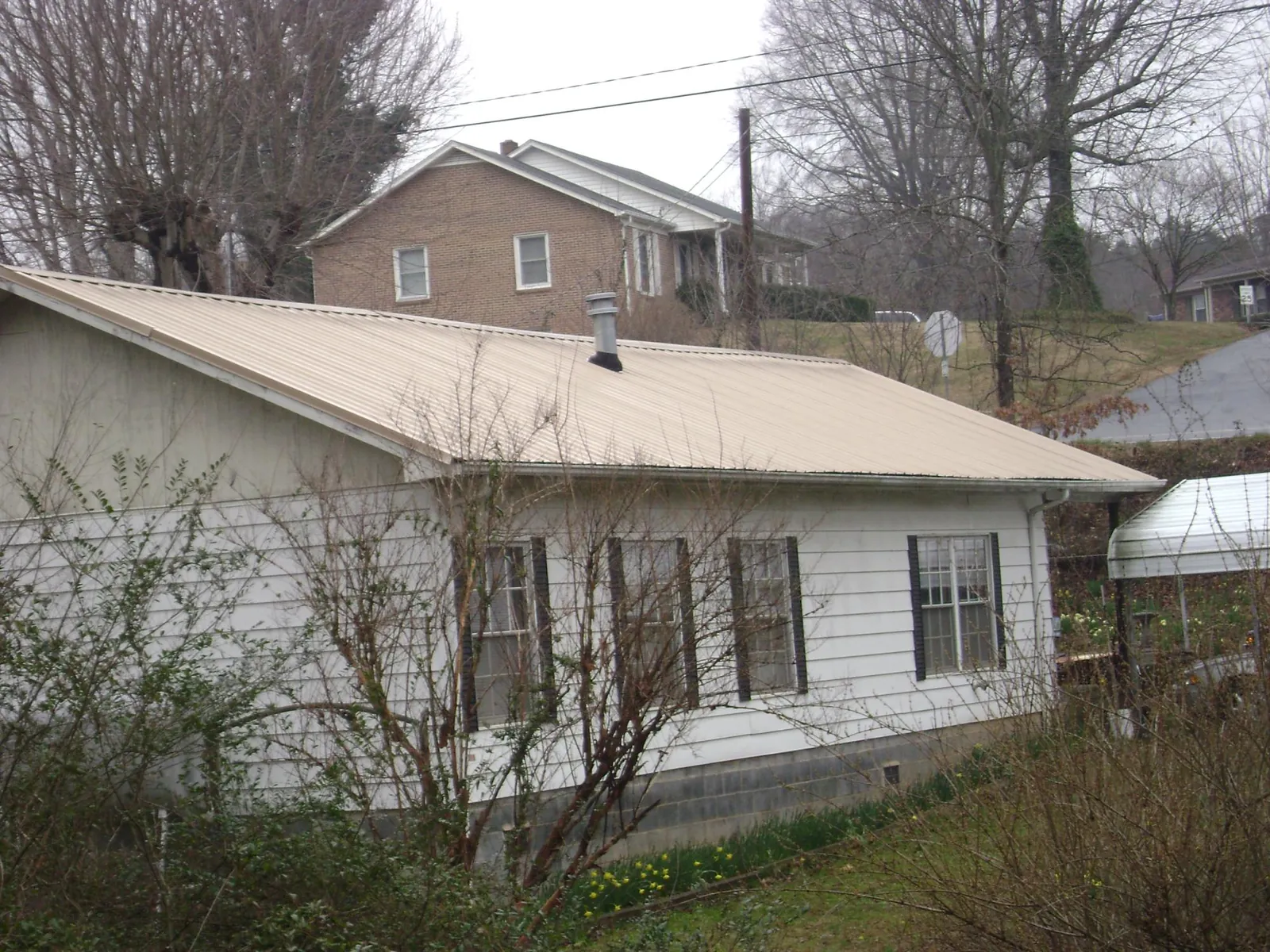 Tan metal roof on a white sided house set into a hillside — Commercial Roofing by Roofing Brothers in Winnett